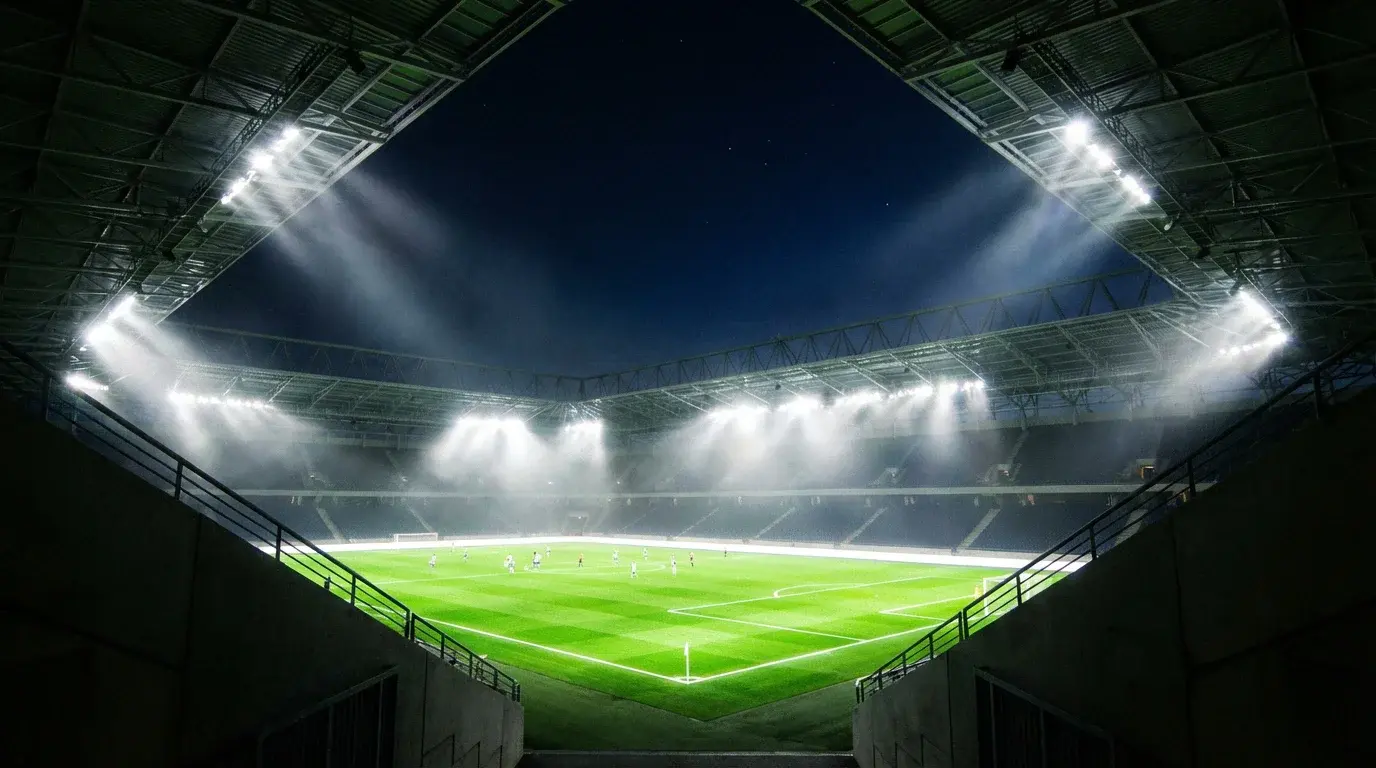 Nogometni stadion ponoči z vklopljenimi reflektorji in osvetljeno zeleno igrišče med tekmo